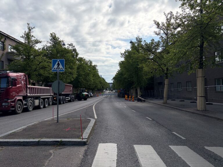 Valokuva. Linnankoskenkatu 1.6.2026 katuremontin aloituspäivänä. Kuvassa näkyy ajorata, jalkakäytävät, katupuita ja työmaa-ajoneuvoja.
